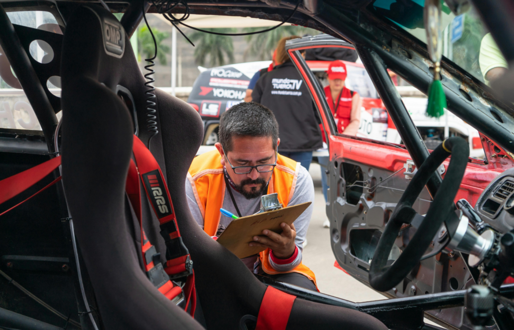 A Man Crouching near a Race Car Writing on a Piece of Paper