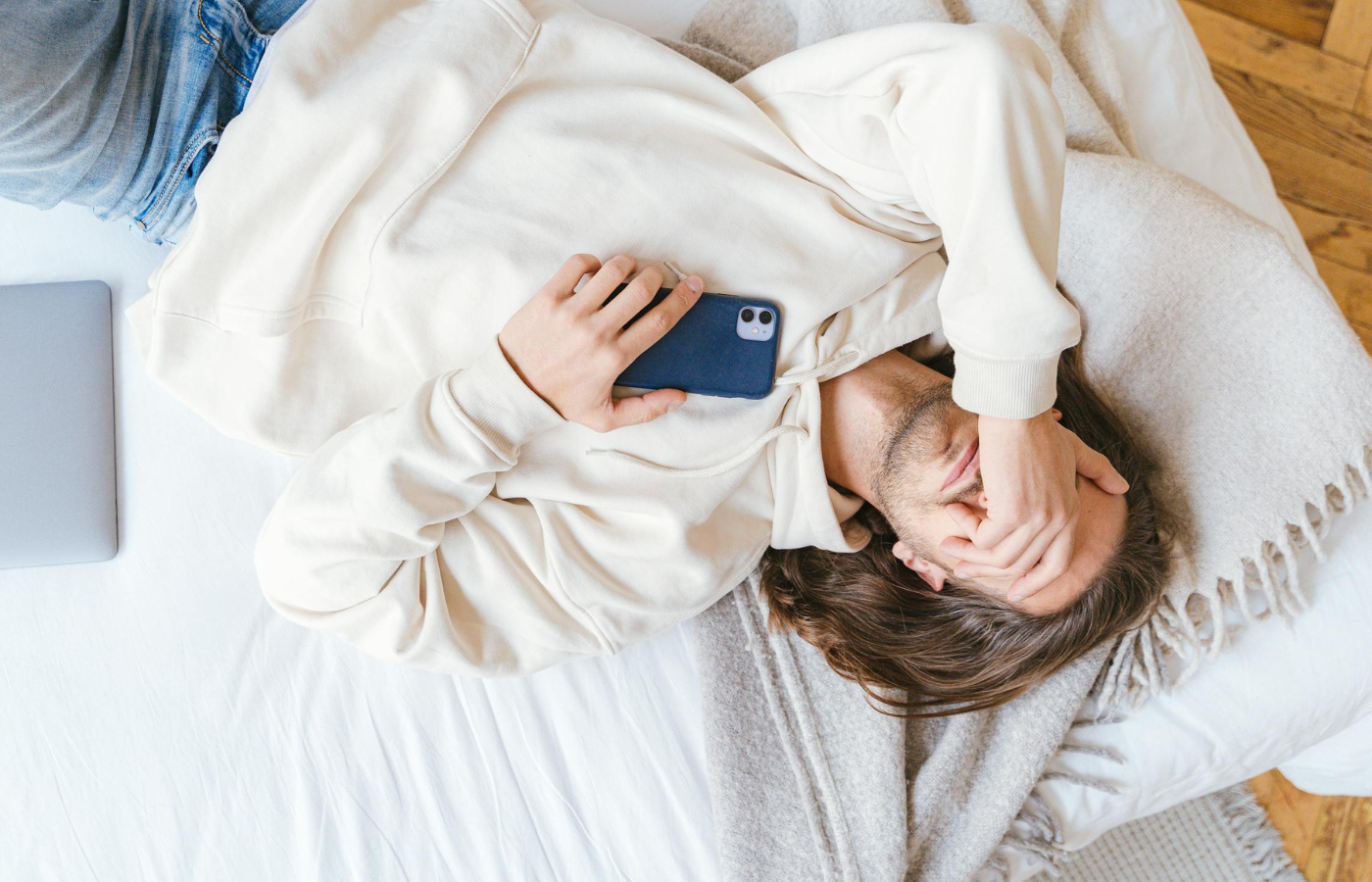 Person lying in bed with a smartphone, looking restless